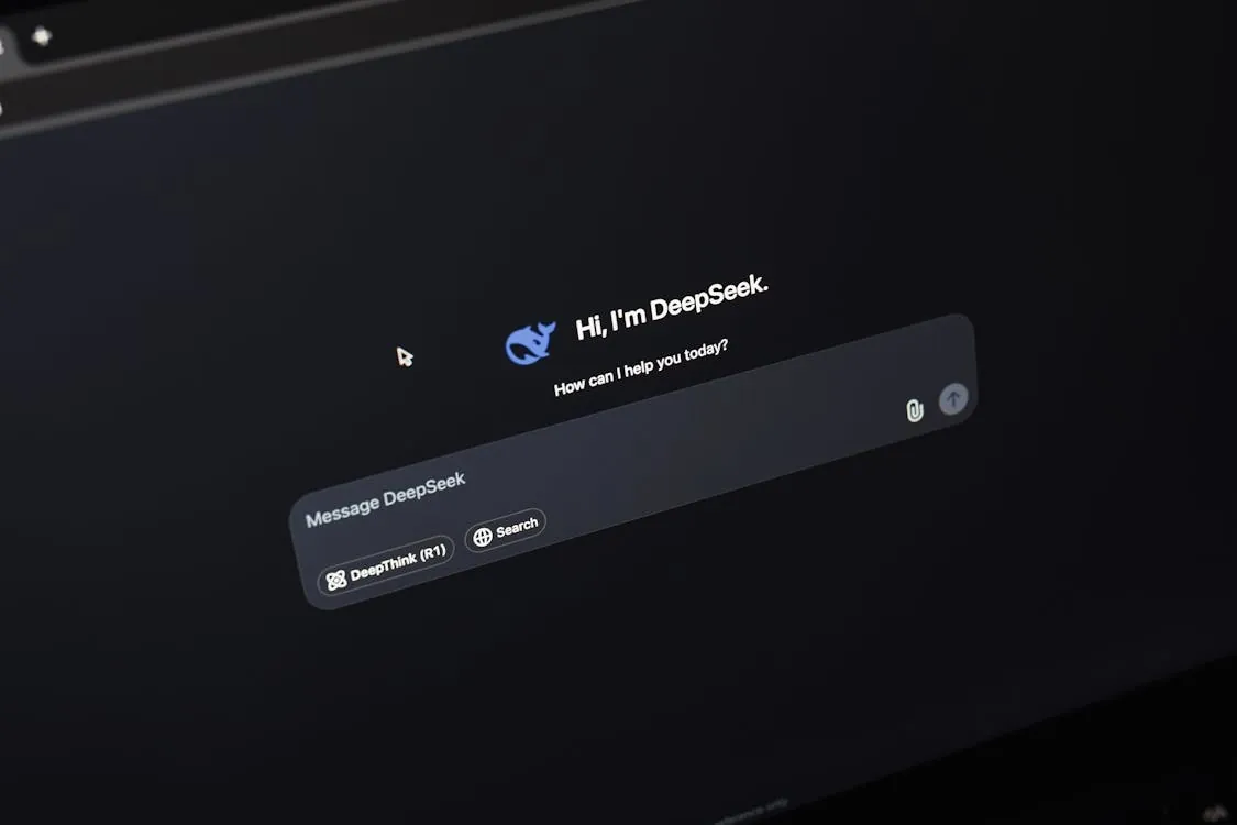 This image shows a computer screen displaying an AI chat interface with a dark background that features a friendly chatbot named DeepSeek, represented by a blue whale icon, welcoming the user and offering assistance. The interface includes options for messaging, searching, and using DeepThink via a controller button, making it suitable for articles about AI conversational tools or virtual assistants.