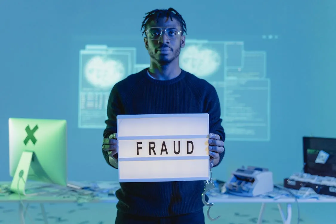 Man holding a 'FRAUD' sign in a tech setting, symbolizing AI-driven cybersecurity threats and the need for security awareness training.