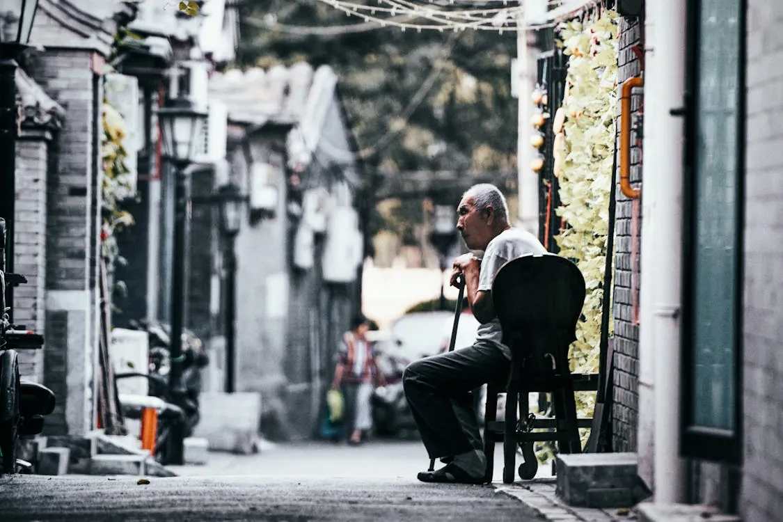 A senior man sits quietly in a historic alley in Beijing, capturing cultural ambiance.