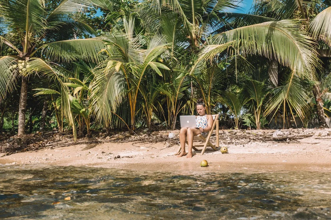 Woman working on a laptop by the beach representing tropical remote work destinations