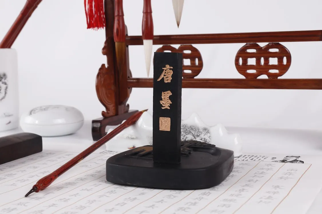 This photo shows a traditional Chinese calligraphy setup, featuring a black ink stone with Chinese characters, a calligraphy brush, and various ink and paper scrolls with Chinese writing, all arranged on a white surface. It highlights the artistic tools and materials used in Chinese calligraphy, making it suitable for articles on Chinese art, calligraphy techniques, or cultural practices.