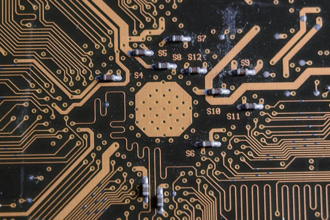 This photo shows a close-up view of a black printed circuit board (PCB) with gold-colored electrical pathways and several electronic components, such as resistors. The setting appears to be a detailed shot of a computer or electronic device's internal circuitry, suitable for articles on electronics, hardware design, or technology manufacturing.