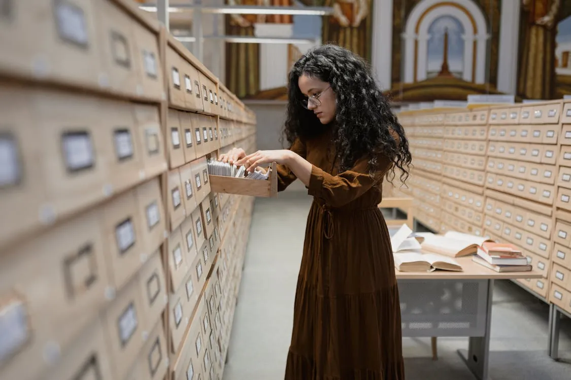 A woman browsing a card catalog in library archives, focusing on research and information gathering.