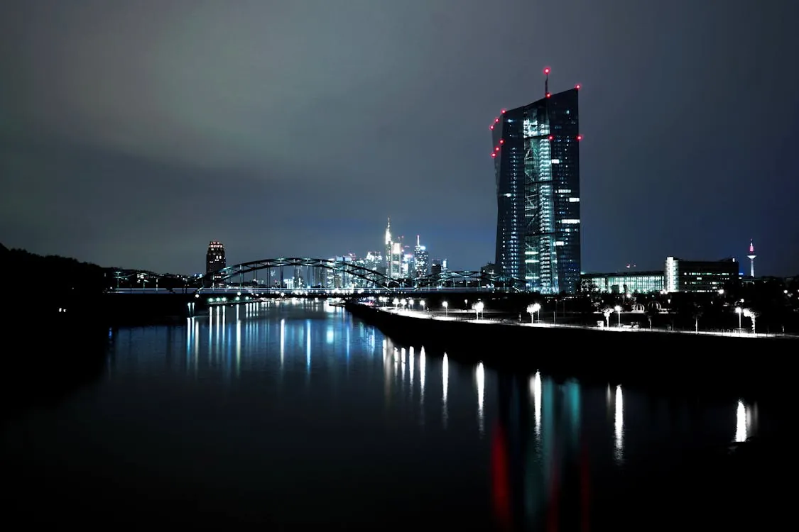 Nighttime skyline with a modern high-rise reflected in a river, representing Frankfurt and European financial centers.