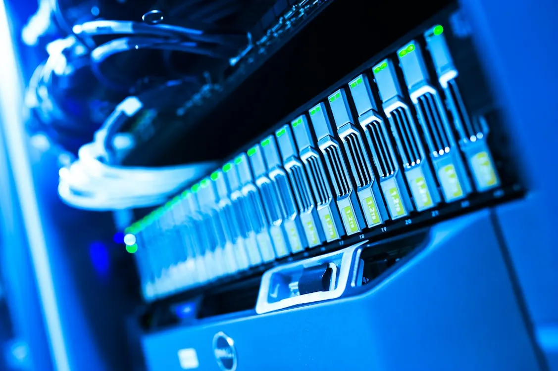 This photo shows a close-up of a server rack filled with multiple illuminated data storage units, with visible cables at the top, set in a dimly lit environment with blue lighting. It is suitable for articles related to data centers, cloud computing, cybersecurity, or technology infrastructure.