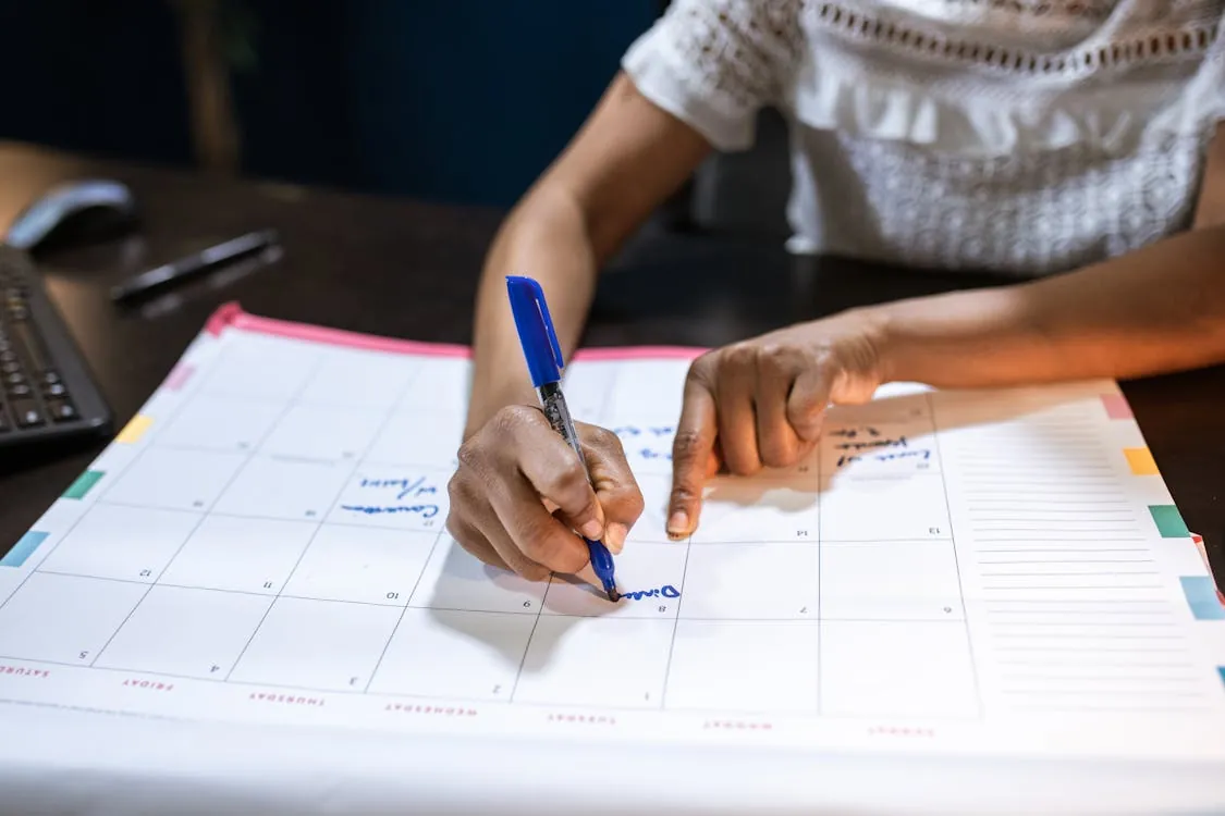 A woman marks important dates on her desk calendar, symbolizing the importance of task scheduling in the evolving web technology landscape of 2026.