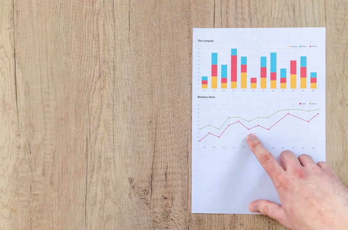 Hand analyzing business graphs on a wooden desk, focusing on data results and growth analysis, representing software benchmarking.