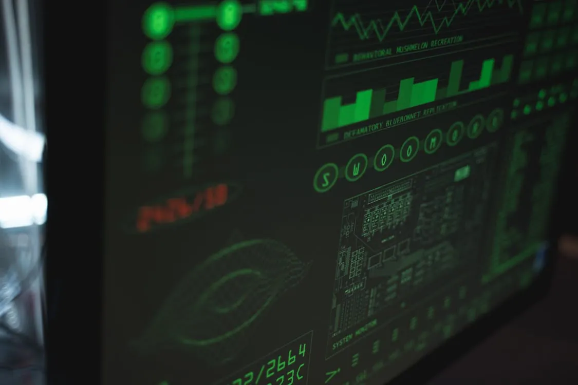 This photo shows a close-up of a dark computer screen displaying various green data visualizations, including graphs, charts, and digital readouts, suggesting activity monitoring, data analysis, or cybersecurity in a high-tech setting. It is suitable for articles related to technology, cybersecurity, data analytics, or digital security themes.