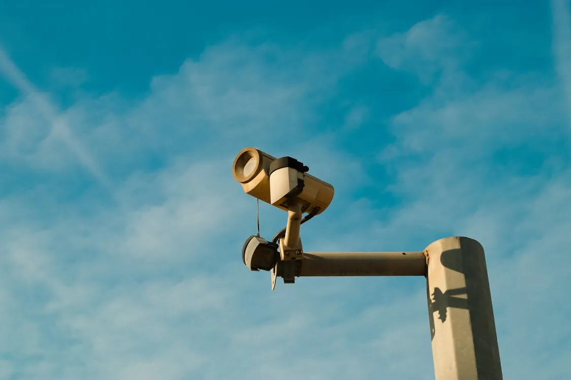 A surveillance camera mounted outdoors against a bright blue sky, symbolizing security and monitoring in a cloud environment.