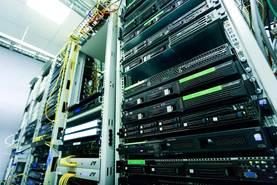 The photo shows a close-up view of a server room or data center, featuring multiple rack-mounted servers, networking equipment, and colorful cables connected to the devices. It highlights the hardware infrastructure typically used for data storage, network management, or cloud computing.