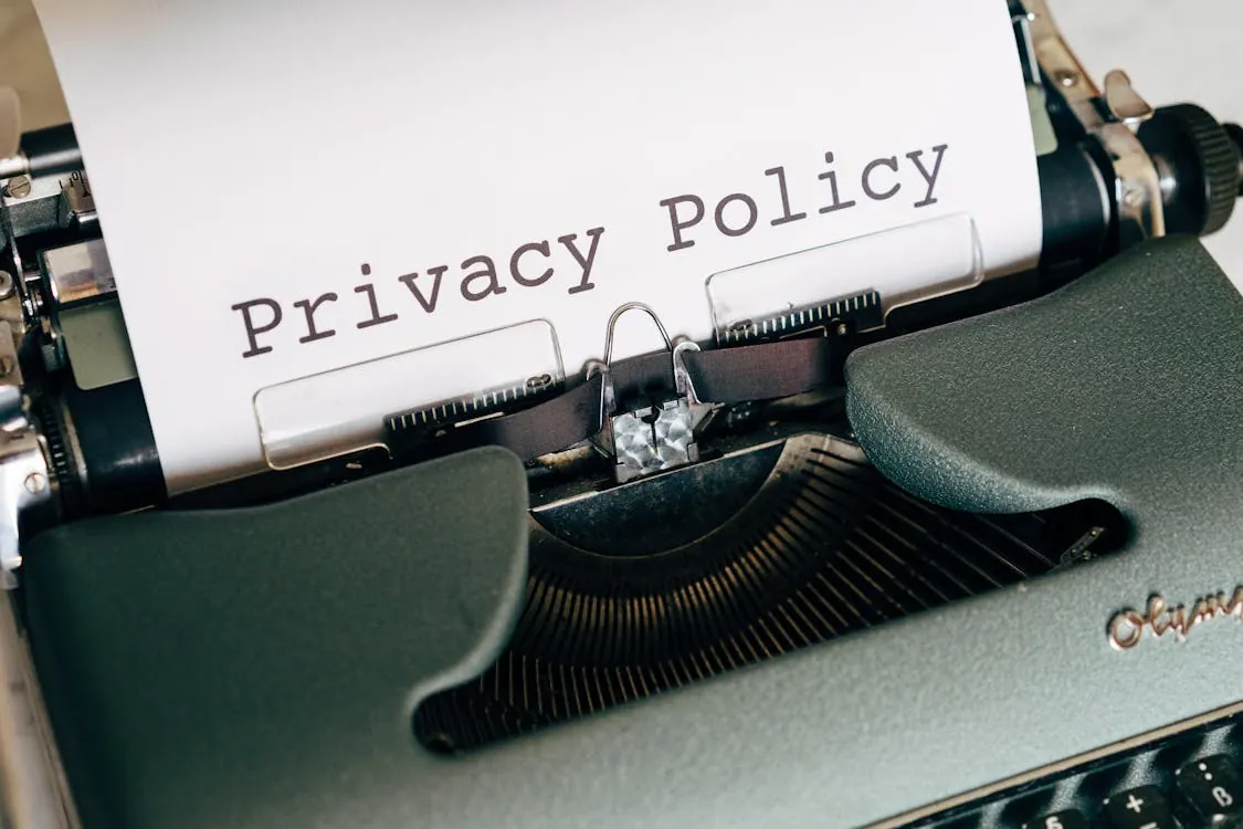 The image shows a vintage typewriter with a sheet of paper inserted, displaying the words "Privacy Policy" in bold, black text, set against a neutral background. It is suitable for articles discussing data protection, online privacy, or legal policies related to information security.