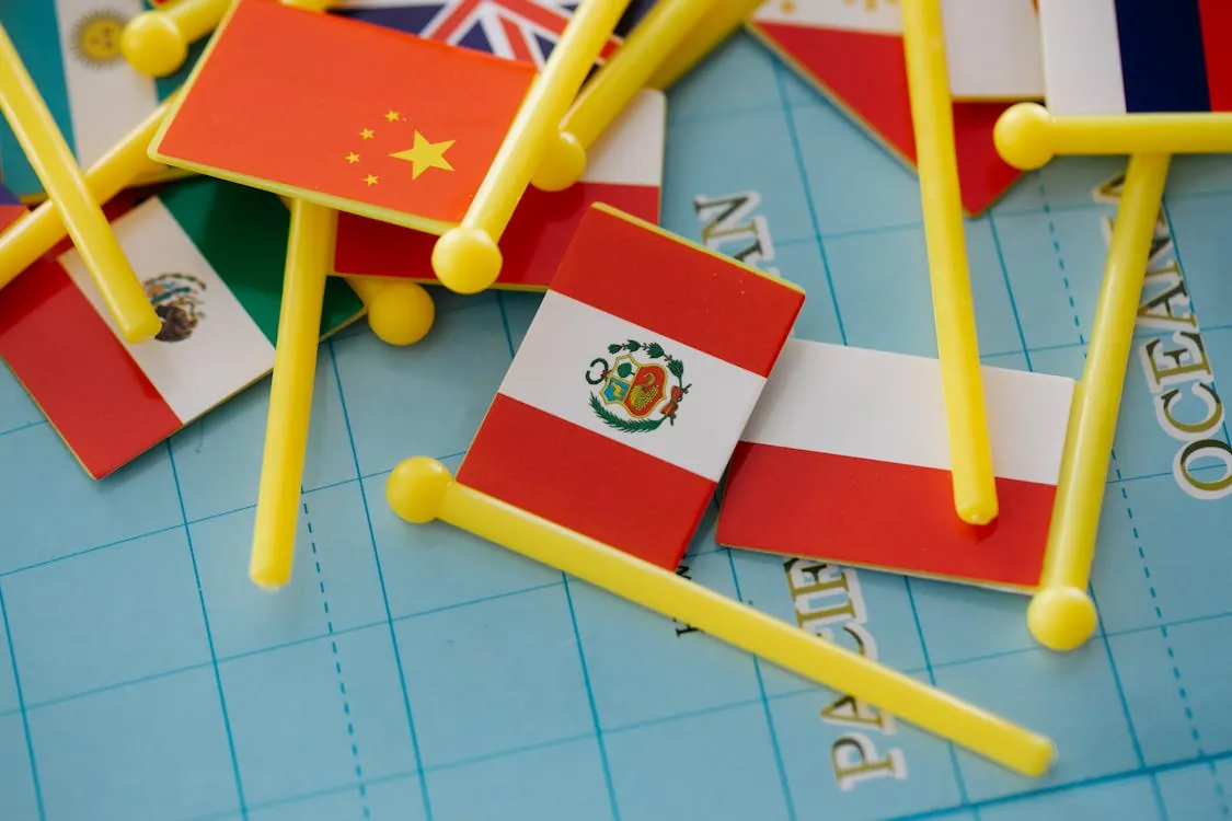 This image features a collection of small flags representing various countries, including China, Peru, the United Kingdom, and Mexico, placed on a world map along with yellow plastic pegs, suggesting an activity related to geography, international relations, or travel planning. The vibrant colors and international theme make it suitable for articles focused on world geography, multicultural awareness, or global connections.