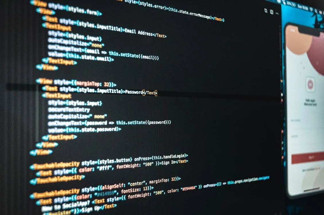 The photo shows a close-up of a computer screen displaying code for a login form, including HTML elements for email and password input fields, with some inline CSS styling, alongside a partially visible interface of a social media or app login page on the right. It would be relevant for articles on web development, UI/UX design, or cybersecurity.