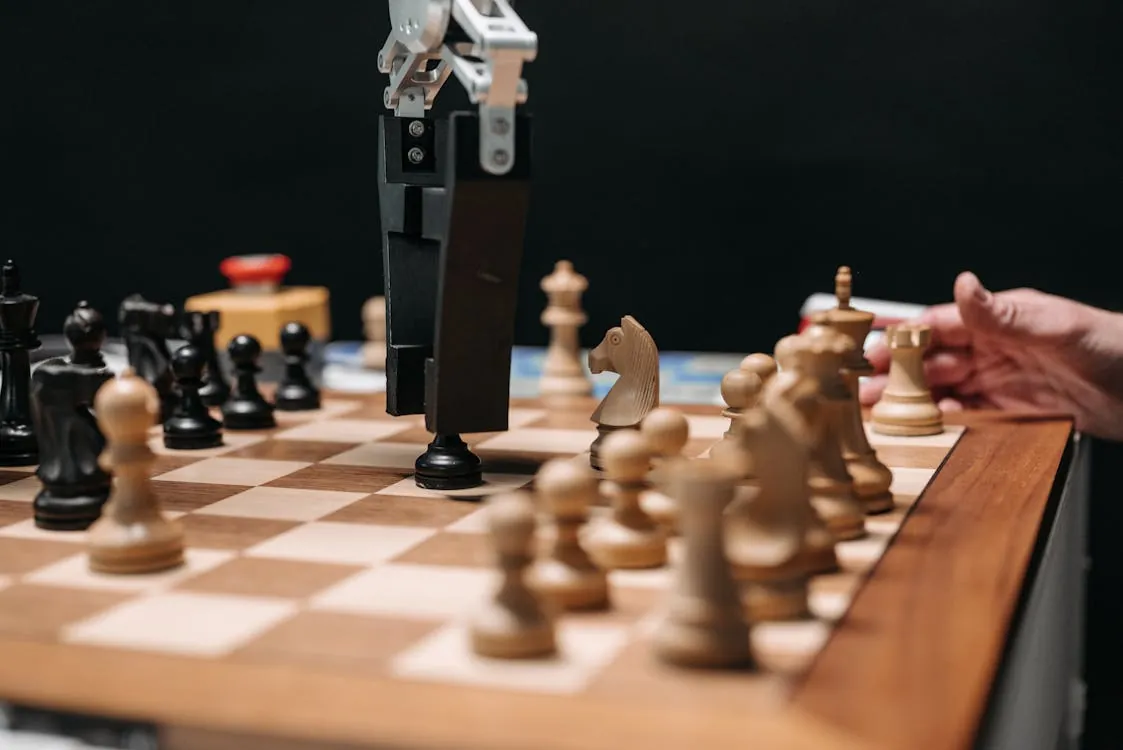 This photo shows a close-up of a chess game in progress, with a focus on the wooden chessboard, chess pieces, and a robotic arm making a move, set against a dark background. It highlights the intersection of technology and traditional board games, making it suitable for articles about AI in gaming, robotics, or modern chess innovations.