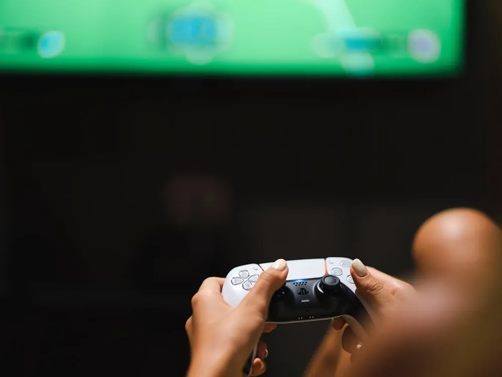 Hands holding a modern game controller in front of a TV showing a game