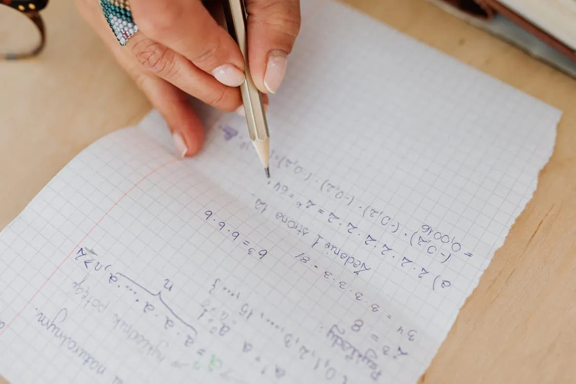 Person handwriting mathematical equations on graph paper