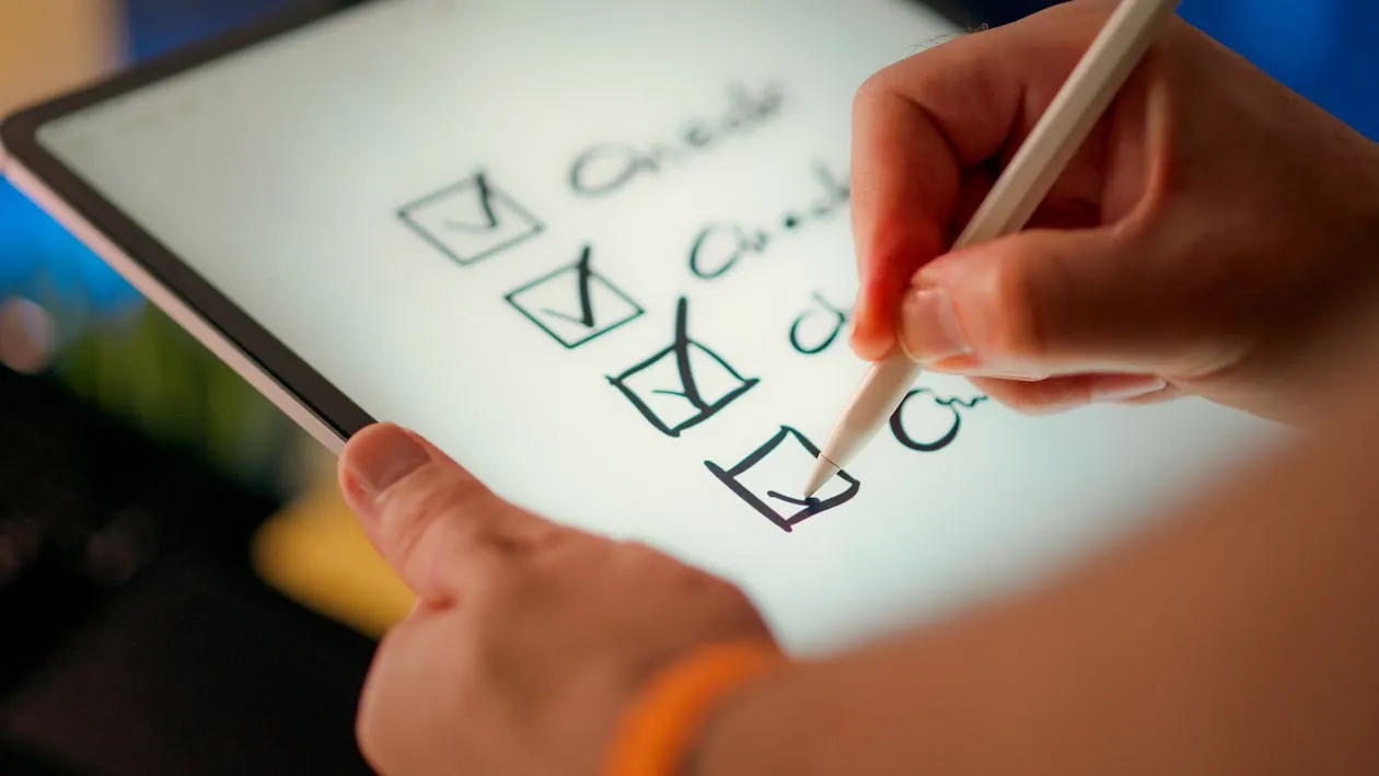 The image shows a person using a stylus to check off items on a to-do list displayed on a digital tablet, with the focus on the hand and the checkmarks next to the listed tasks. This setting suggests productivity, task management, or organization themes suitable for articles about planning or digital tools.