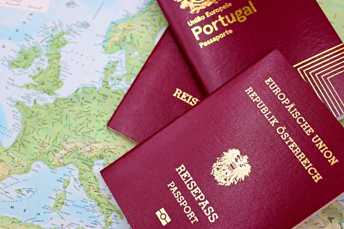 This photo shows two Portuguese passports placed on a map of Europe, suggesting travel or planning a trip within or from Europe. The passports are prominently displayed, with noticeable gold lettering, indicating the subject of international travel or immigration.
