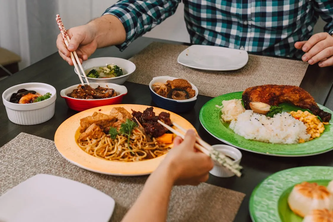 A variety of Asian and Italian dishes presented beautifully on a wooden table, showcasing diverse flavors.