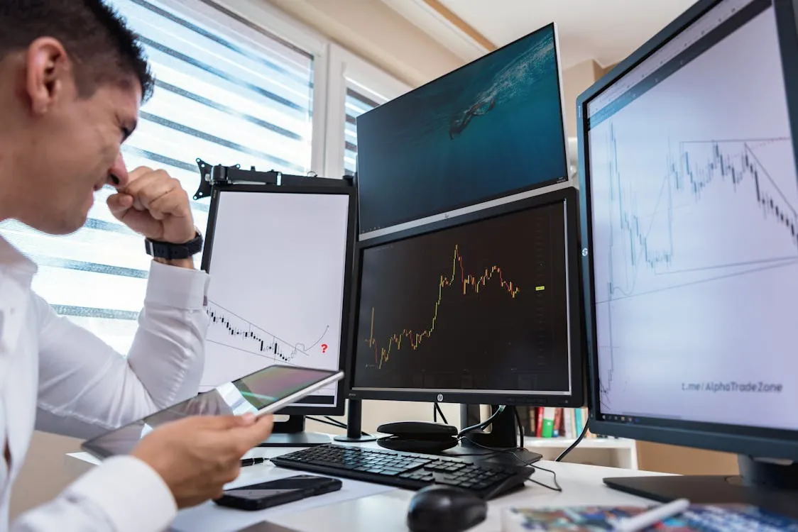 Trader analyzing stock charts on multiple monitors