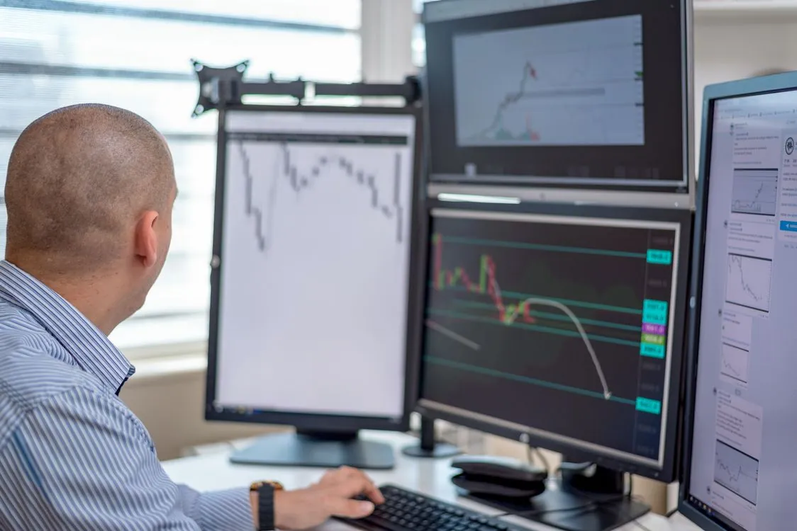 Person analyzing data on multiple computer monitors showing charts and AI performance metrics