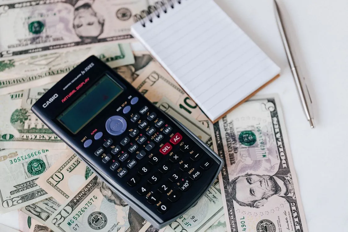 Calculator and notepad on US dollar bills representing AI fine-tuning cost analysis