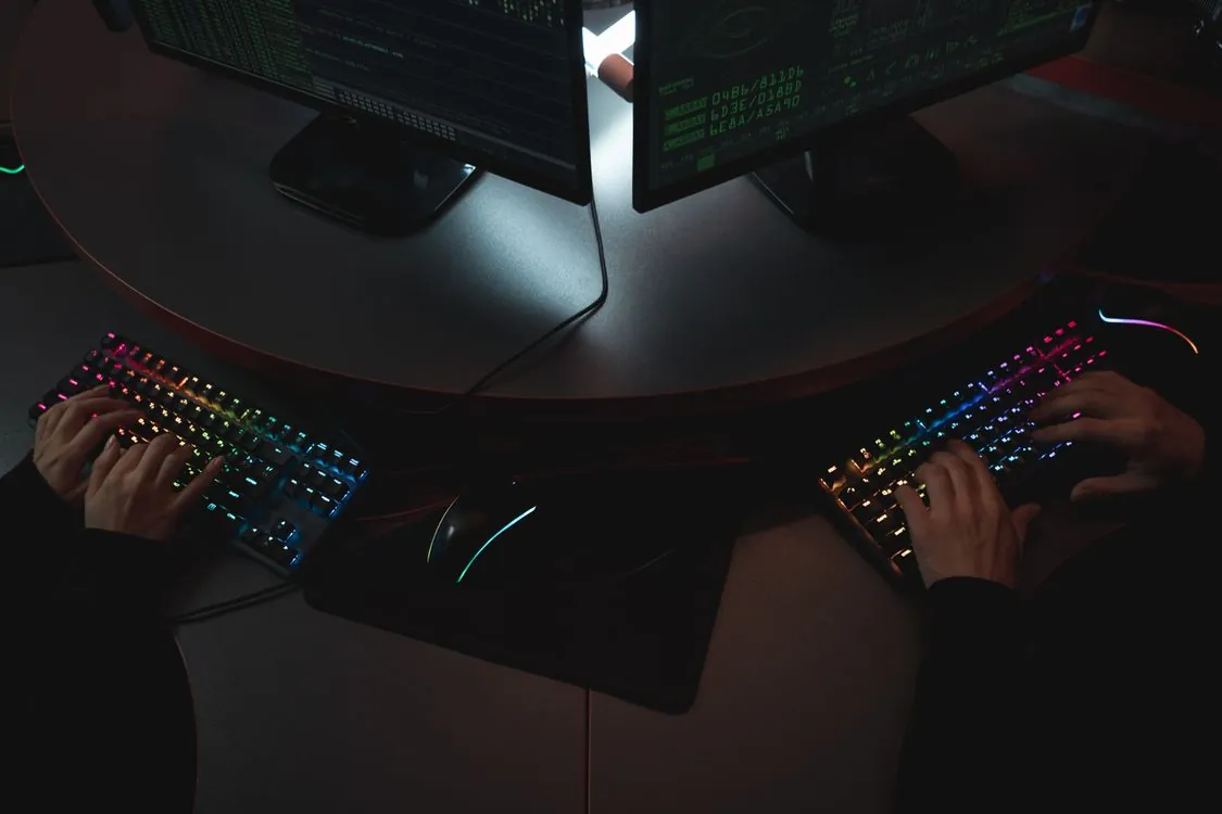 Two people monitoring code and data on dual screens in a dimly lit security environment